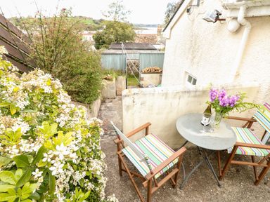A small outdoor patio area with two striped chairs and a round table with flowers and wine at Seabien in Falmouth