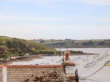 View of a harbor with numerous sailboats on the water grassy hills with trees in the background and a rooftop with antennas and cables in the foreground at Seabien in Falmouth
