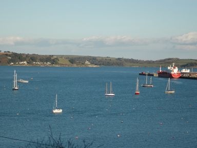 A harbor with multiple sailboats and a large red ship docked at a pier with green hills in the background at Seabien in Falmouth