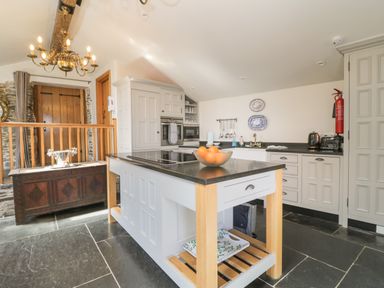 A kitchen with a central island holding a bowl of oranges Chandler cabinets and wooden beams at Glanville House Mevagissey