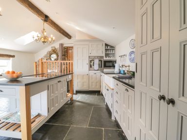 A kitchen with a central island, white cabinets, stone floor, and exposed wooden beams at Glanville House in Mevagissey