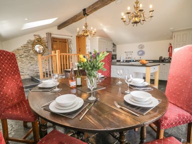 A dining area with a round wooden table set for four with red upholstered chairs a kitchen and wooden door in the background at Glanville House in Mevagissey