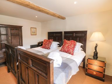 A bedroom with twin wooden beds red pillows a wooden wardrobe a bedside table with a lamp and a wooden beam on the ceiling at Glanville House in Mevagissey