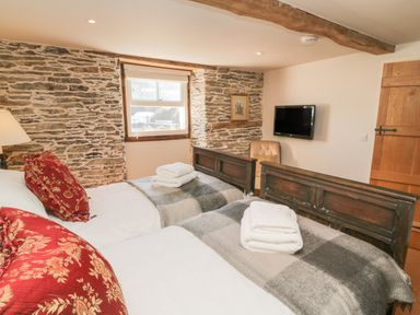 A bedroom with two single beds with folded towels on blankets and a television on the wall at Glanville House in Mevagissey