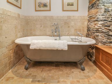 A clawfoot bathtub with a towel draped over the edge and tiled walls and floor in a bathroom at Glanville House Mevagissey
