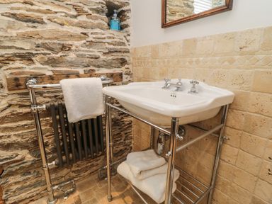 A bathroom sink with towels on a rack and stone walls at Glanville House in Mevagissey