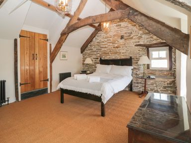 A bedroom with a bed towels bedside lamps wooden beams and a stone wall at Glanville House in Mevagissey