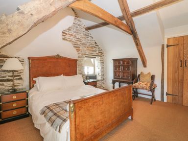 A bedroom with wooden bed frame side tables lamps and exposed wooden beams at Glanville House in Mevagissey