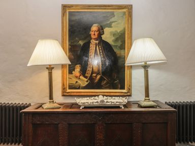 A framed portrait above a wooden sideboard with two table lamps and a decorative tray at Glanville House Mevagissey