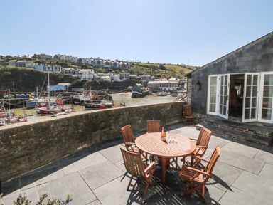 An outdoor patio with wooden table and chairs overlooking a harbor with boats and hillside houses at Glanville House in Mevagissey