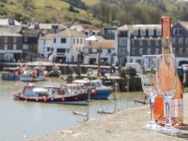 A bottle of rose wine and two wine glasses on a stone ledge overlooking a harbor with boats and buildings in the background at Glanville House in Mevagissey