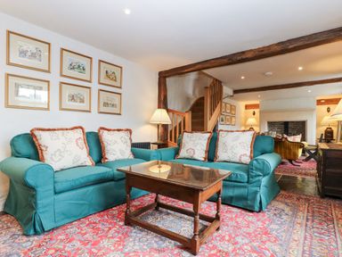 A living room with two teal sofas a wooden coffee table framed pictures on the wall and exposed wooden beams at Glanville House in Mevagissey