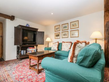 A sitting room with teal sofas a wooden coffee table a dark wooden cabinet with a television and framed pictures on the wall at Glanville House in Mevagissey