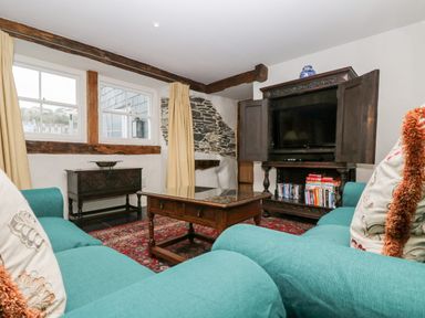 A living room with turquoise sofas a wooden coffee table a TV in a wooden cabinet and exposed stone and wooden beams at Glanville House in Mevagissey