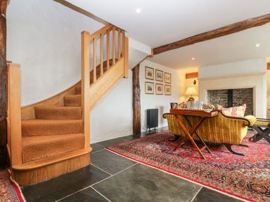 A living room with wooden stairs a fireplace and a red patterned rug at Glanville House in Mevagissey