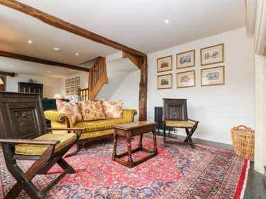 A living room with wooden chairs a yellow striped sofa a wooden coffee table and framed pictures on the wall at Glanville House in Mevagissey