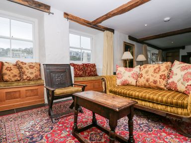 A living room with a patterned rug a wooden coffee table a sofa with floral cushions and a wooden armchair at Glanville House in Mevagissey