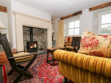 A living room with a fireplace wooden chairs a wooden coffee table and a patterned rug at Glanville House in Mevagissey