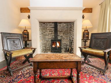 A room with a stone fireplace a wood stove two carved wooden chairs a wooden table and two lamps at Glanville House Mevagissey