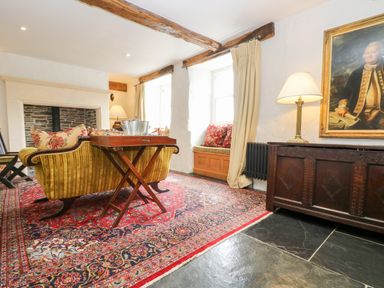 A living room with a yellow sofa a wooden table a red patterned rug and a painting on the wall at Glanville House Mevagissey