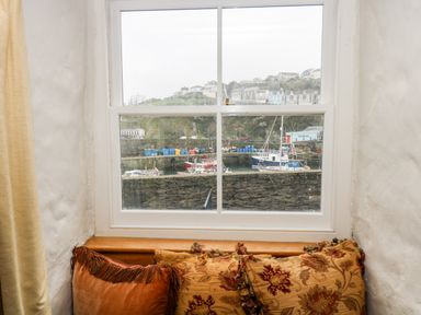 A window seat with cushions and a view of boats and houses outside at Glanville House in Mevagissey