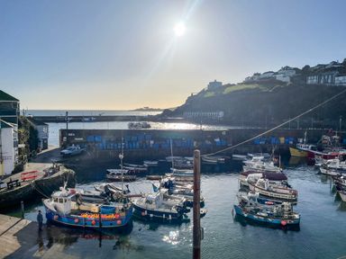 A harbor with boats docked and buildings on a hill overlooking the water at Glanville House in Mevagissey