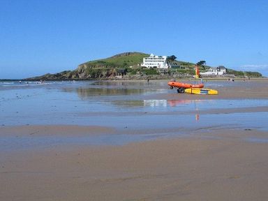 A sandy beach with a small boat and people in the water near a hill with white buildings at Glebe House in Bigbury
