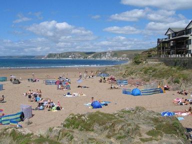 A sandy beach with people sunbathing and playing near the sea with cliffs and a building on the right at Glebe House in Bigbury