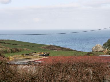 A coastal landscape with green fields ocean in the background and rooftops in the foreground at Gurnard's Cottage in St Ives