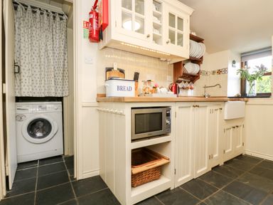 A kitchen with microwave oven bread box and sink next to a washing machine behind a curtain at Gurnard's Cottage in St Ives
