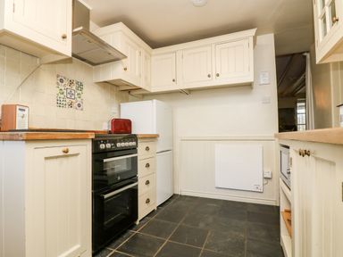 A kitchen with cream cabinets a black oven a white refrigerator and a red toaster at Gurnard's Cottage in St Ives