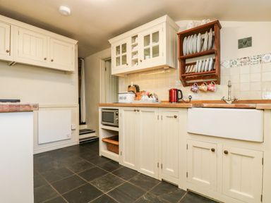 A kitchen with cream cabinets wooden countertops a microwave red kettle and a dish rack at Gurnard's Cottage in St Ives