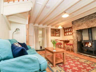 A living room with a blue sofa a wooden coffee table with flowers a stone fireplace and a dining table with chairs at Gurnard's Cottage in St Ives