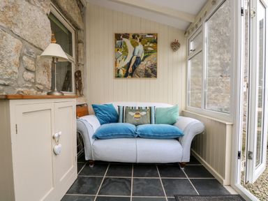 A small sitting area with a sofa and cushions next to a cabinet with a lamp at Gurnards Cottage in St Ives