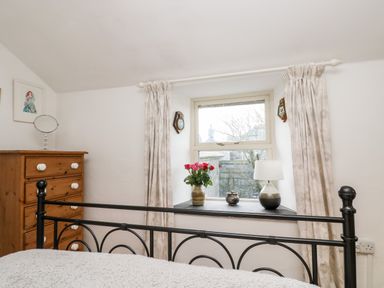 A bedroom with a black metal bed frame wooden chest of drawers and a window with flowers on the sill at Gurnards Cottage in St Ives