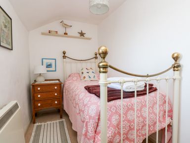 A bedroom with a single bed with brass bed frame pink patterned bedspread and wooden nightstand with lamp at Gurnard's Cottage in St Ives