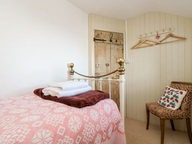 A bedroom with a patterned bedspread folded towels on the bed a vintage wooden door a chair with a cushion and wall hooks with clothes hangers at Gurnard's Cottage in St Ives