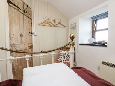 A bedroom with a metal bed frame towels on the bed a wooden door and hangers on a wall rack at Gurnard's Cottage in St Ives
