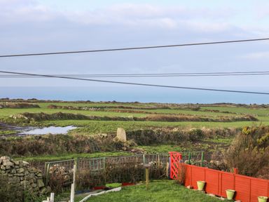 A coastal view with green fields separated by stone walls and a red fence in the foreground at Gurnard's Cottage in St Ives