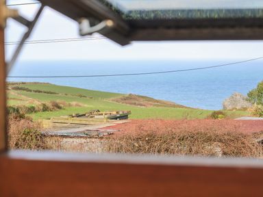 A view of green fields and the sea beyond seen through a wooden window frame at Gurnards Cottage in St Ives