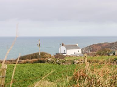A white house near the coastline with green fields in the foreground at Gurnard's Cottage in St Ives