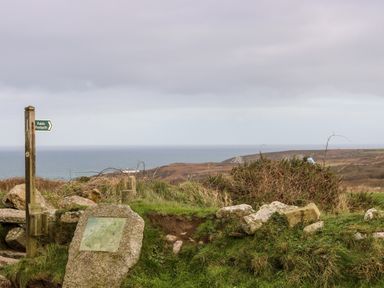 A rural coastal landscape with a public footpath sign and an informational stone at Gurnard's Cottage in St Ives