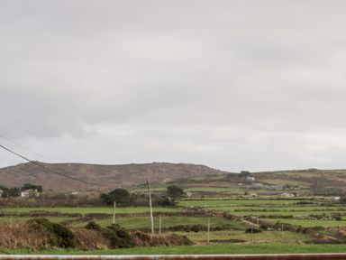 A rural landscape with green fields stone walls and hills under a cloudy sky at Gurnard's Cottage in St Ives