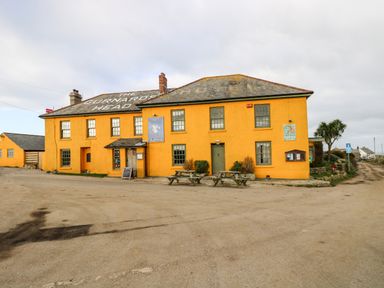 A large yellow building with multiple windows and picnic tables outside on a dirt road at Gurnard's Cottage in St Ives