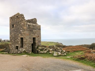 An old stone ruin building near the coast with grassy land and the sea in the background at Gurnard's Cottage in St Ives