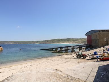 A beach with a boat ramp and boats near a stone building by the sea at Gurnard's Cottage in St Ives