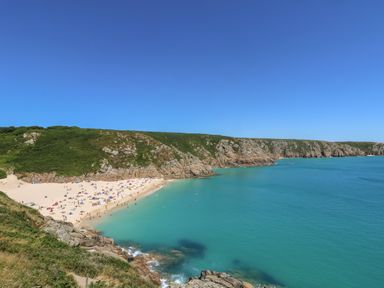 A sandy beach with people swimming and sunbathing near rocky cliffs and blue ocean water at Gurnard's Cottage in St Ives
