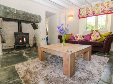A living room with a wood stove fireplace wooden coffee table with flowers and a sofa with cushions at Parwin Tintagel