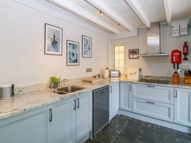 A kitchen with light blue cabinets, granite countertops, stainless steel sink, dishwasher, toaster, kettle, stove with stainless steel hood, and pictures on the wall at Parwin in Tintagel
