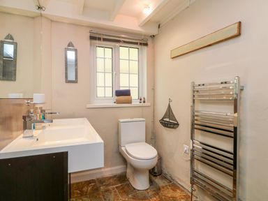 A bathroom with a toilet, double sink, window with folded towels, towel rack, and a wall-mounted decorative sailboat at Parwin in Tintagel